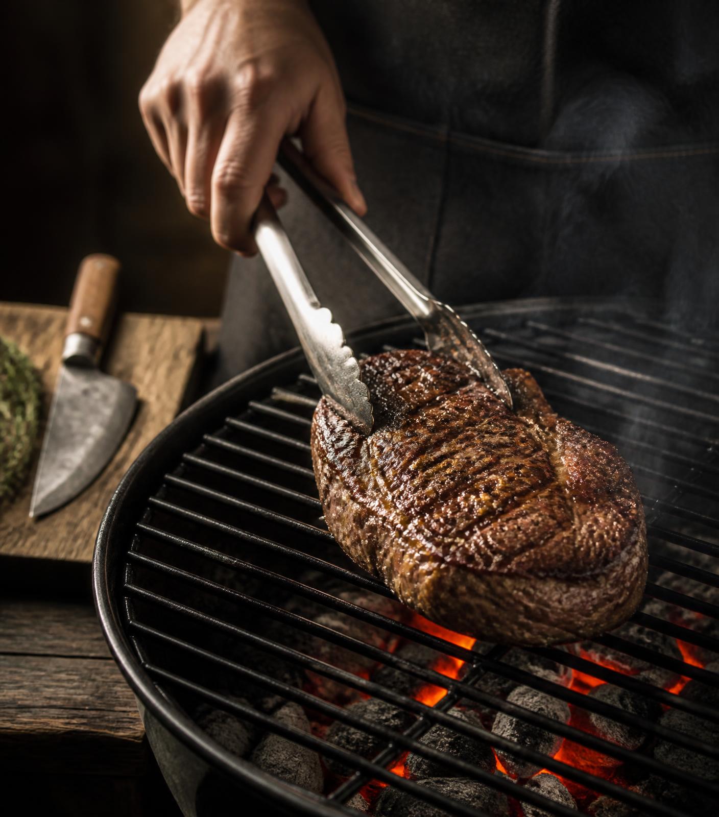 Mão virando a carne na grelha sobre a brasa